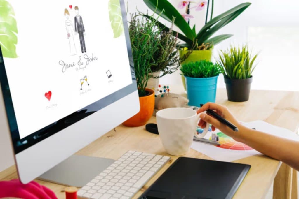 Desktop monitor showing a wedding website design, with plants and a coffee mug on the desk