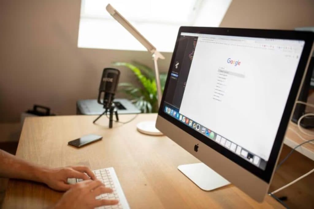 Person typing at an iMac showing Google search, with a microphone on the desk