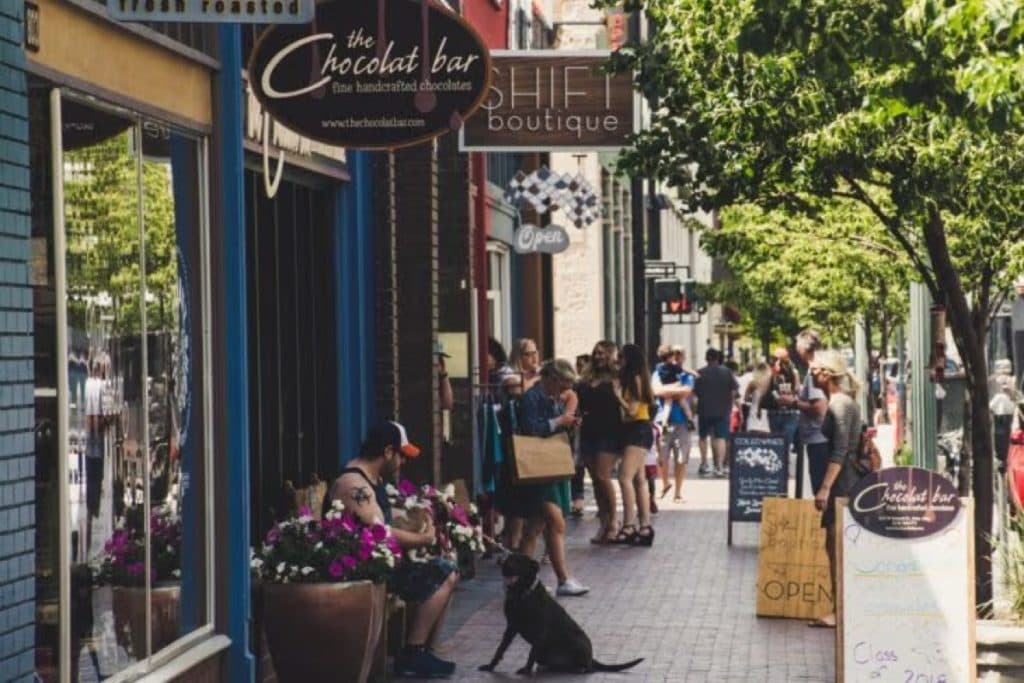 Shoppers walking along a busy downtown street lined with boutiques and a chocolate shop